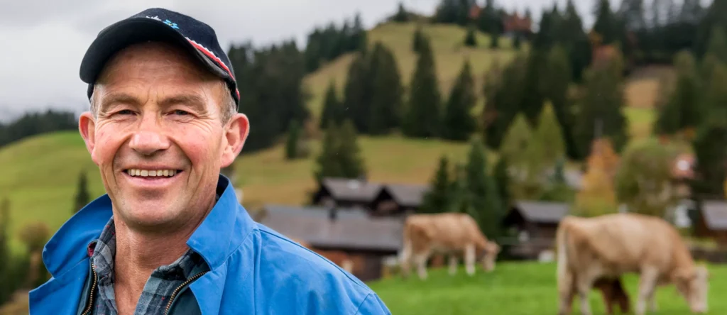 En mann som smiler foran kyr, og demonstrerer generasjonsskiftet i oppdrett.
