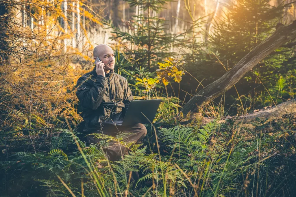 En mann som jobber på en bærbar PC i skogen mens han anmelder årsberetning.
